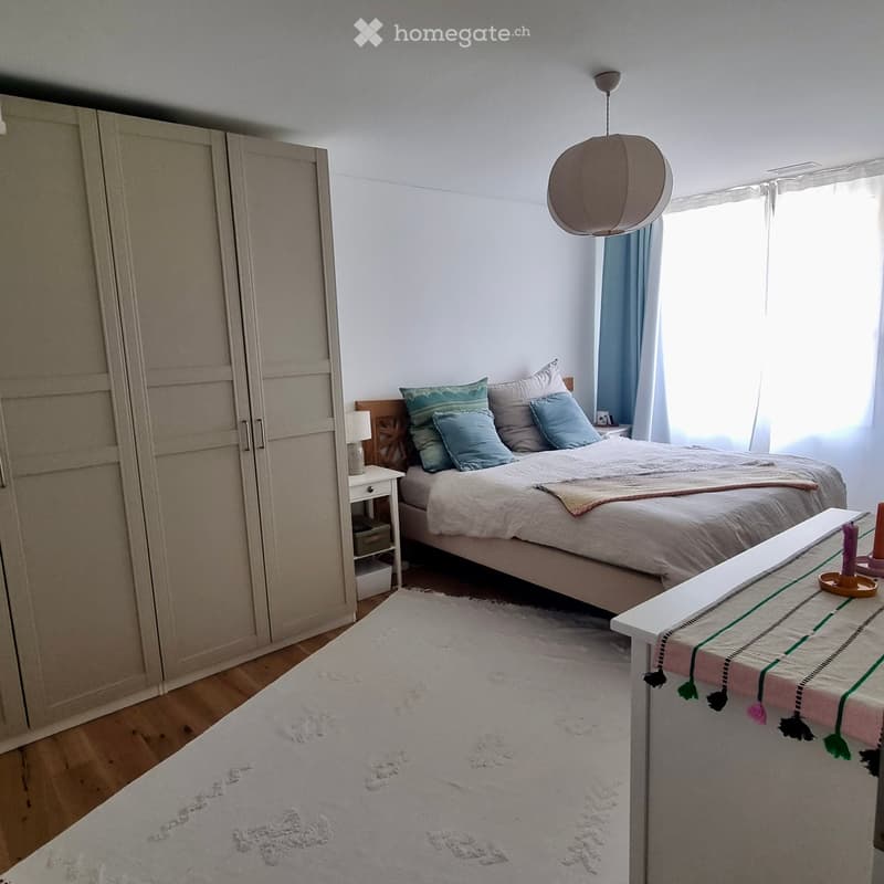 Cozy bedroom with a large bed, nightstand, wardrobe, and a white rug on the floor.