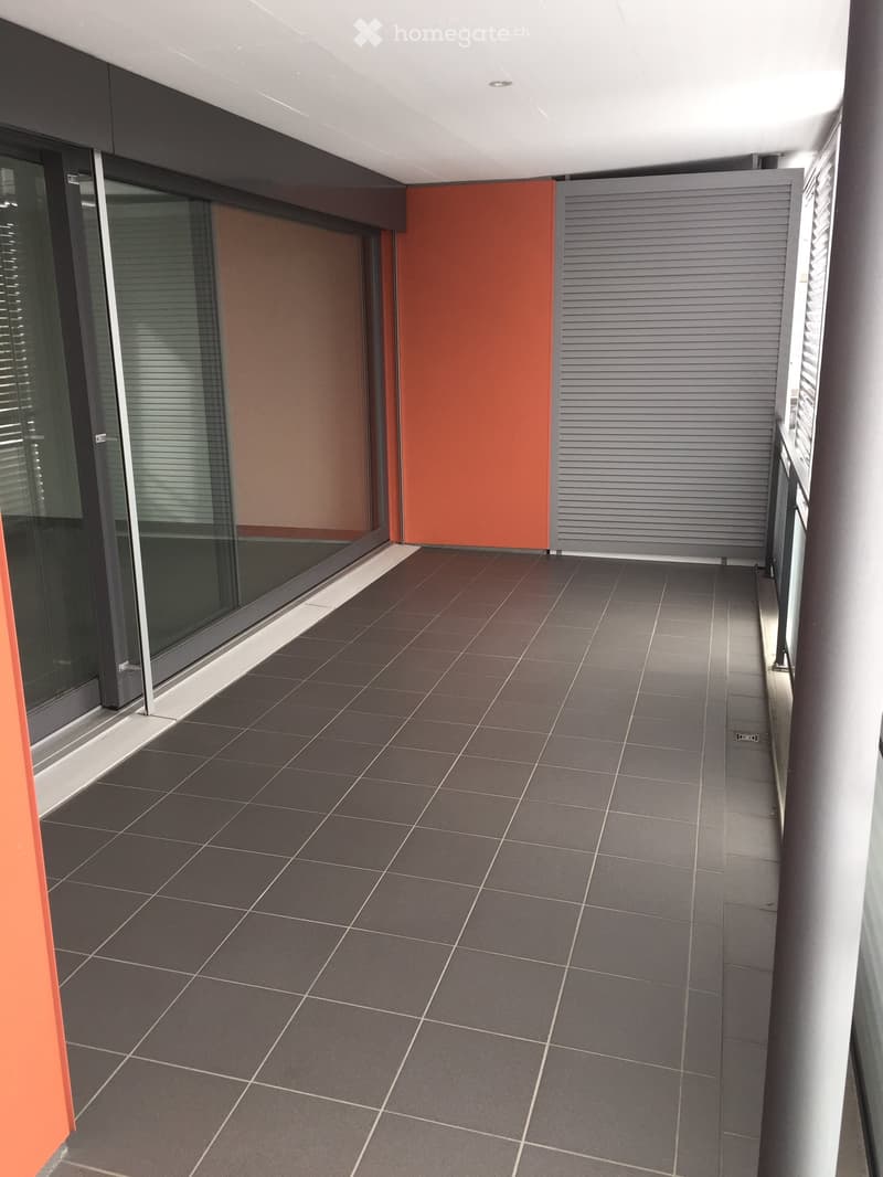 Modern balcony with dark grey tiled flooring, glass sliding doors, and grey shutters.