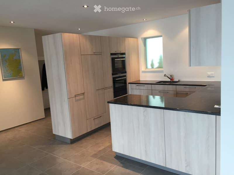 Modern kitchen with light wood cabinets, black countertop, sink, and built-in oven. Features recessed lighting and a small window above the sink.