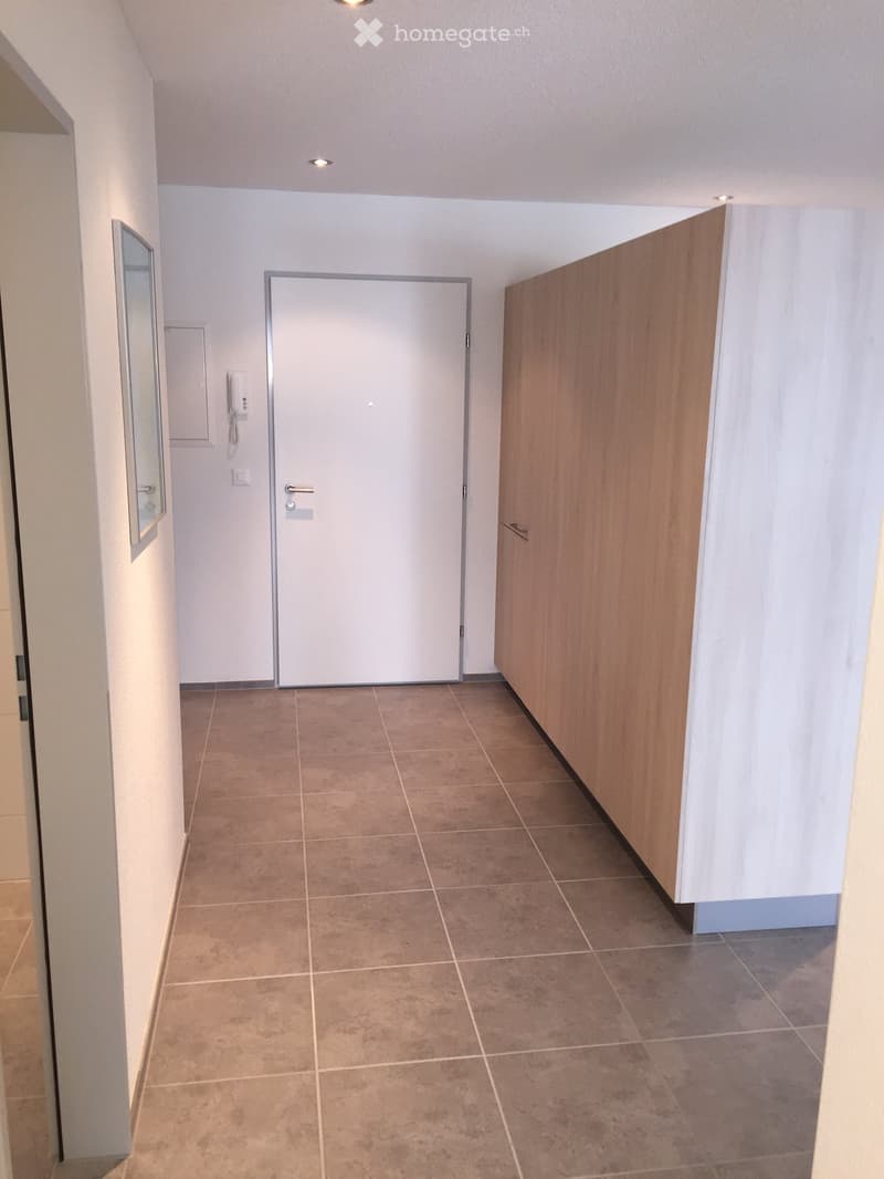 Empty hallway with tiled floor, white walls, and two doors, one wooden and one white, with a small mirror on the left wall.