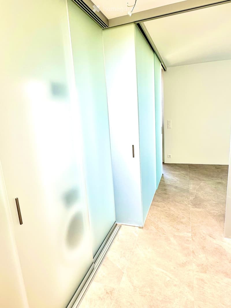 Empty hallway with light-colored walls, tiled floor, and a partially open door leading to another room.