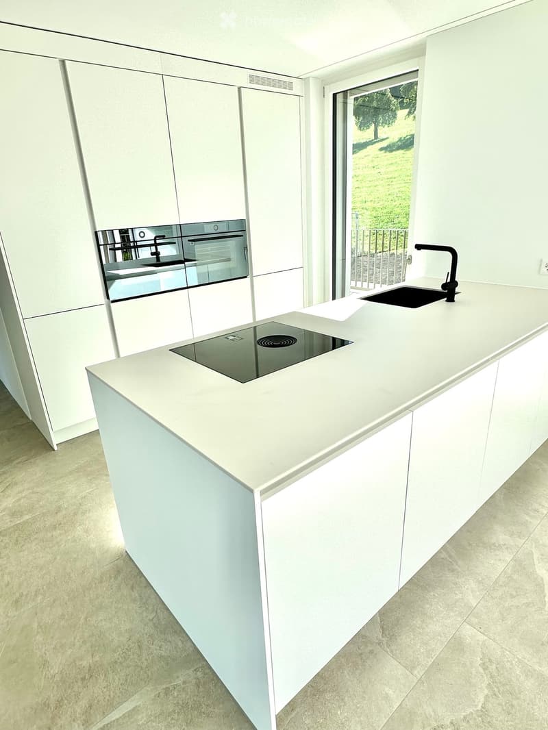 Modern kitchen with a white island featuring an induction cooktop, a sink with a black faucet, and white cabinets.