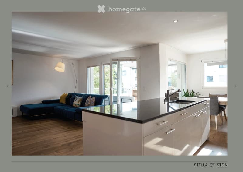 Open-plan living and kitchen area with a dark blue sofa, kitchen island, and modern fixtures.