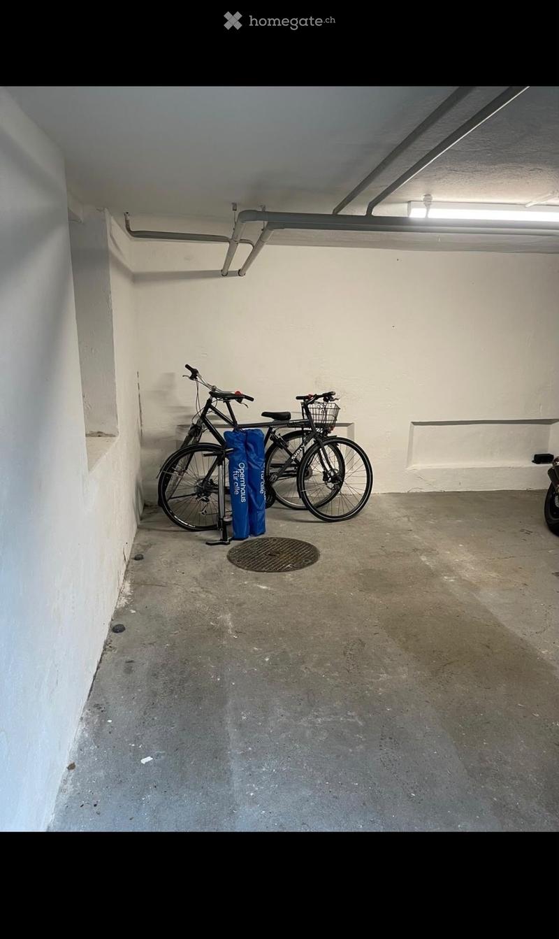 Underground parking space with concrete floor, white walls, and two bicycles parked against the wall.