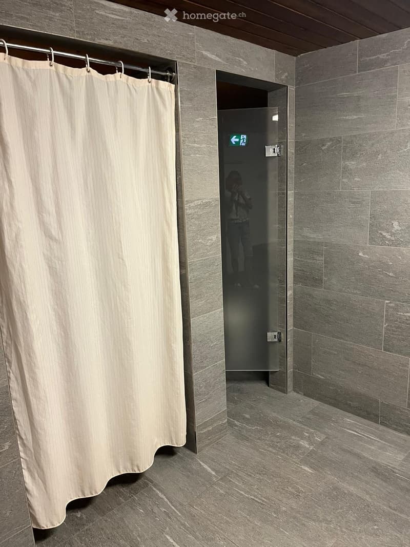 Modern bathroom with grey tiled walls and floor, featuring a shower curtain and a glass-enclosed shower area.