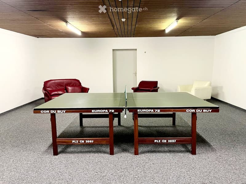 A room with a table tennis table, two red chairs, and a white sofa.