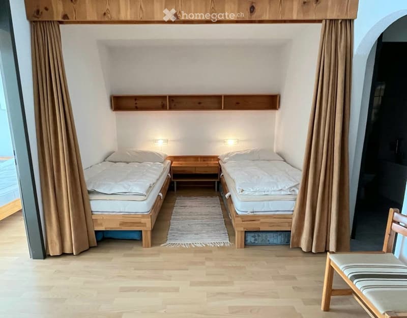 Cozy bedroom with two single beds, wooden nightstand, small chair, and built-in wooden shelves above the beds.