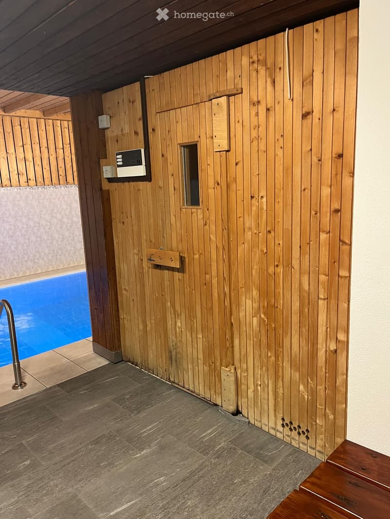 Wooden sauna room with tiled floor, control panel, small window, and adjacent swimming pool area.