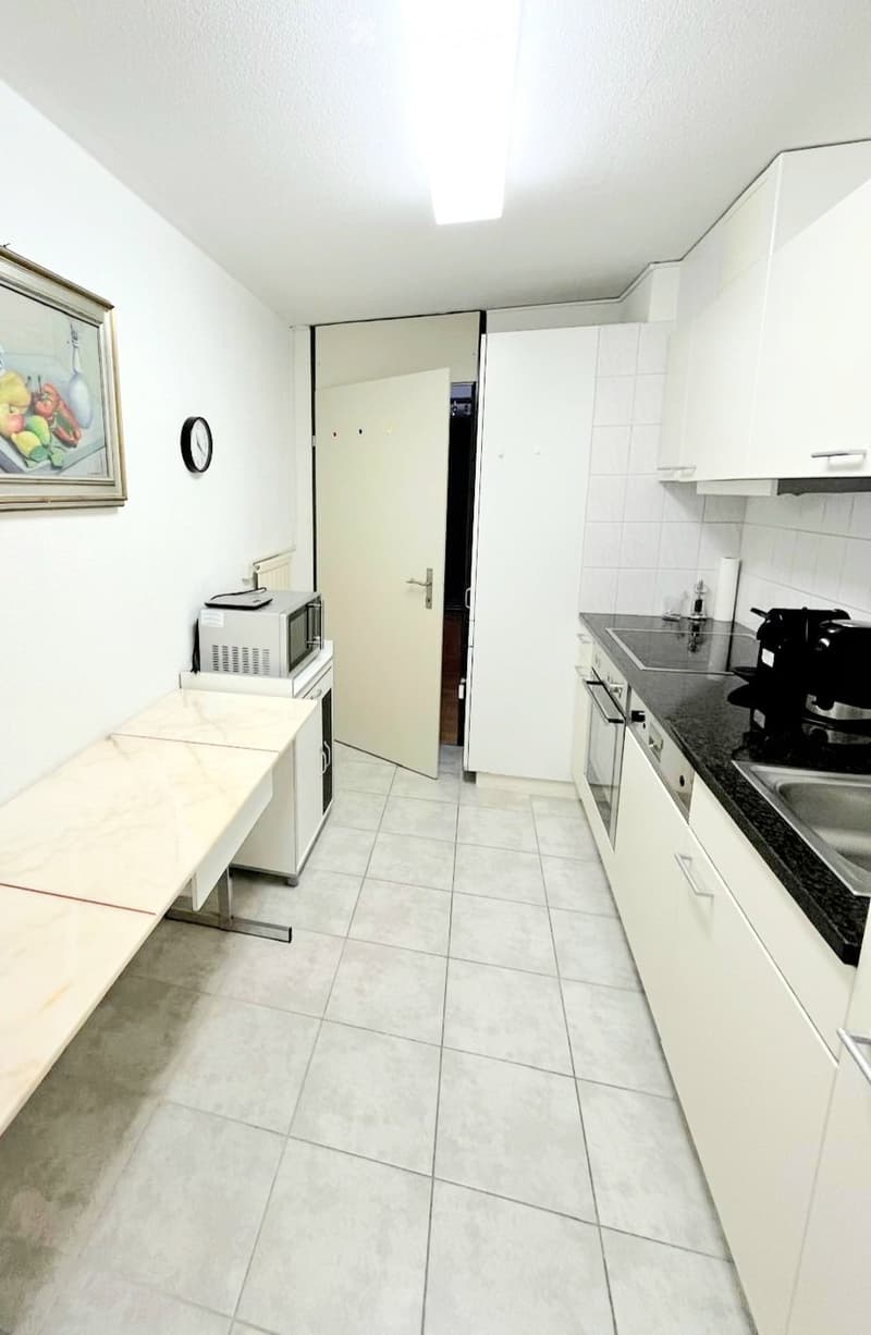 Modern kitchen with white cabinets, tiled floor, microwave, coffee maker, and a small table.