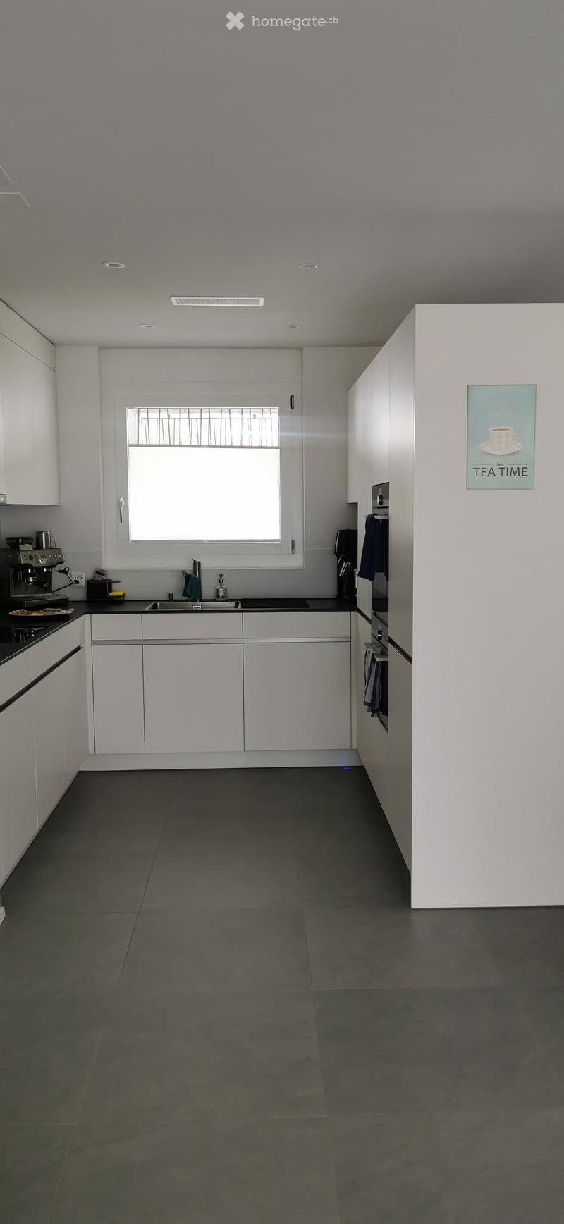 Modern kitchen with white cabinets, dark countertops, and a large window. Features a coffee maker, sink, and a poster on the wall.