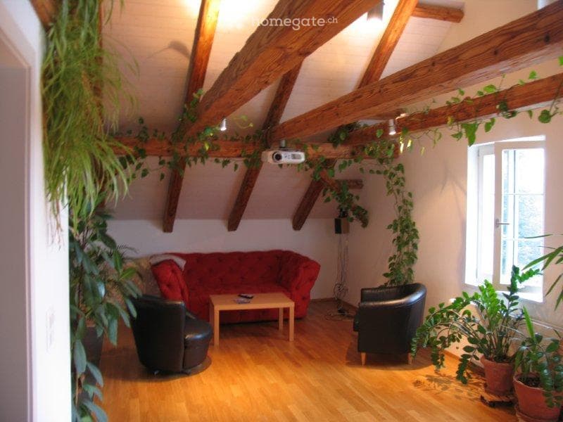 Living room with wooden beams, red sofa, coffee table, armchairs, projector, and potted plants.