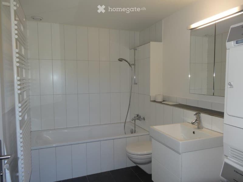 Modern bathroom with white tiles, bathtub, toilet, sink, mirror, and showerhead.