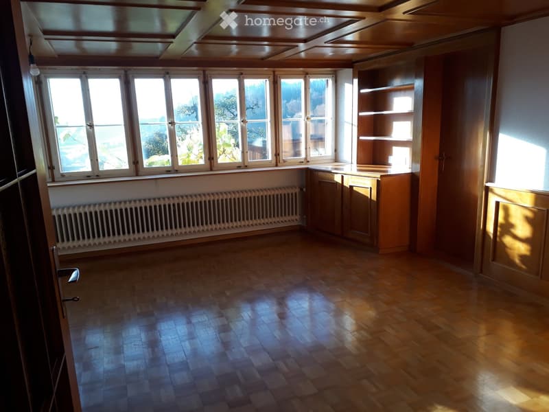 Empty room with wooden flooring, large windows, built-in cabinetry, and radiator. No furniture or personal items present.
