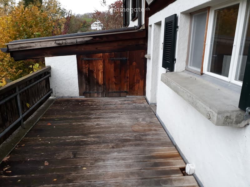 Wooden balcony with railing, wooden door, and view of autumn foliage.