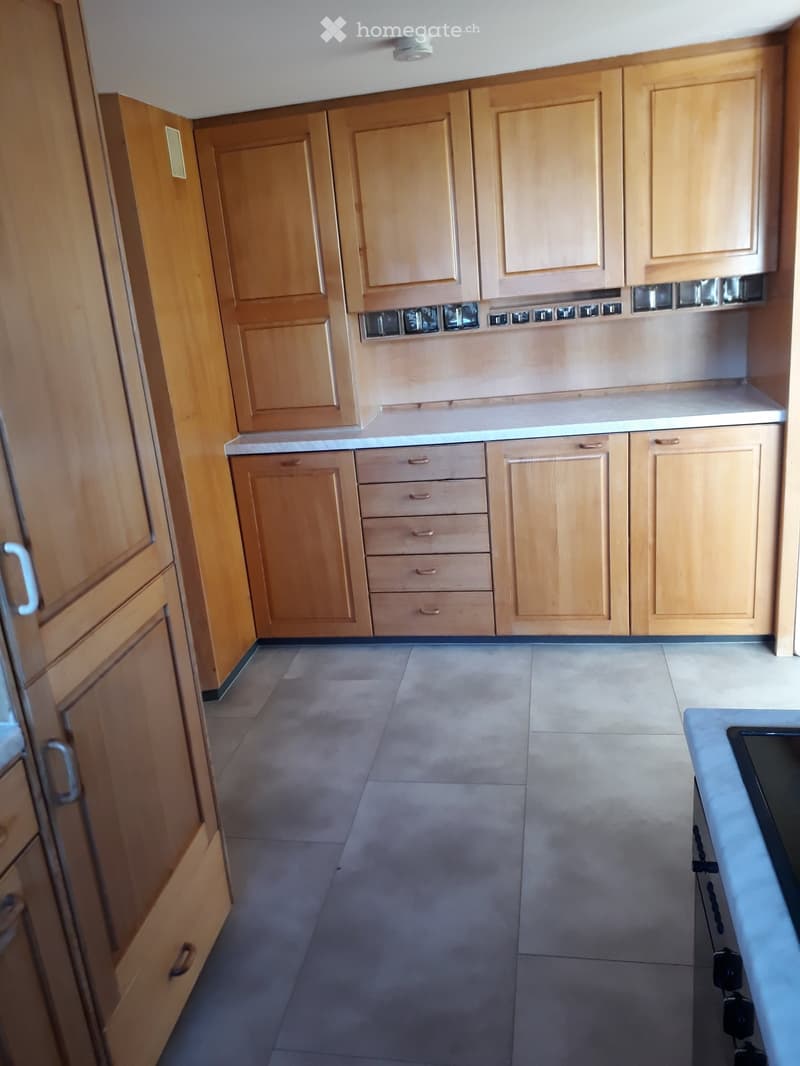 Empty kitchen with light wooden cabinets and drawers, tiled floor, and a countertop visible on the right side.