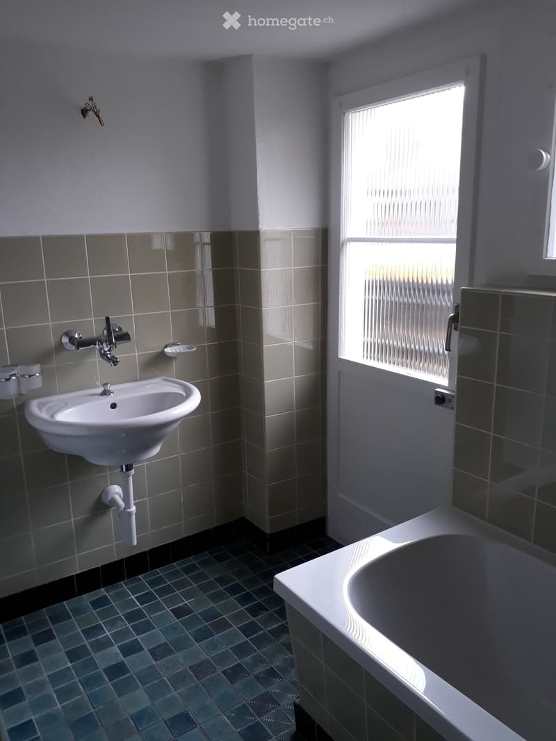 Bathroom with a white sink, faucet, and bathtub, featuring tiled walls and a window with blinds.