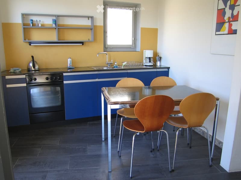 Modern kitchen with blue cabinets, stainless steel oven, sink, coffee maker, and a dining table with chairs.