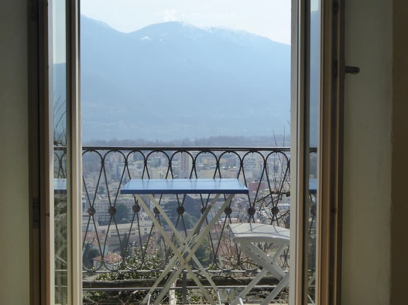 Balcony with a view of a cityscape and mountains, featuring a small table and a chair.