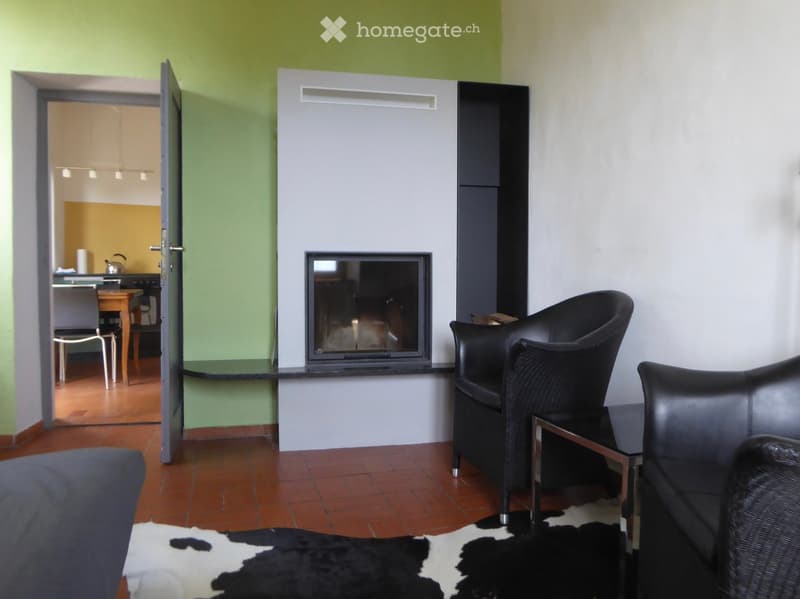 Living room with a fireplace, sofa, chair, small table, and a stool. The room has a modern design with a mix of black and white decor, including a cowhide rug on the floor.