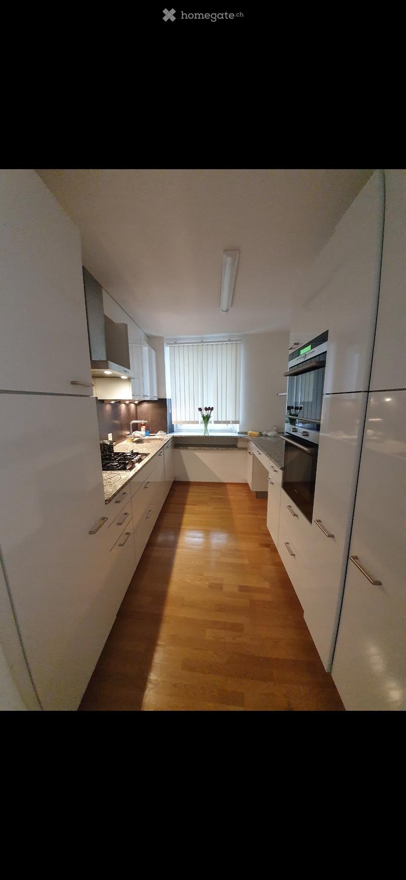 Modern kitchen with white cabinets, stainless steel appliances, and a wooden floor.