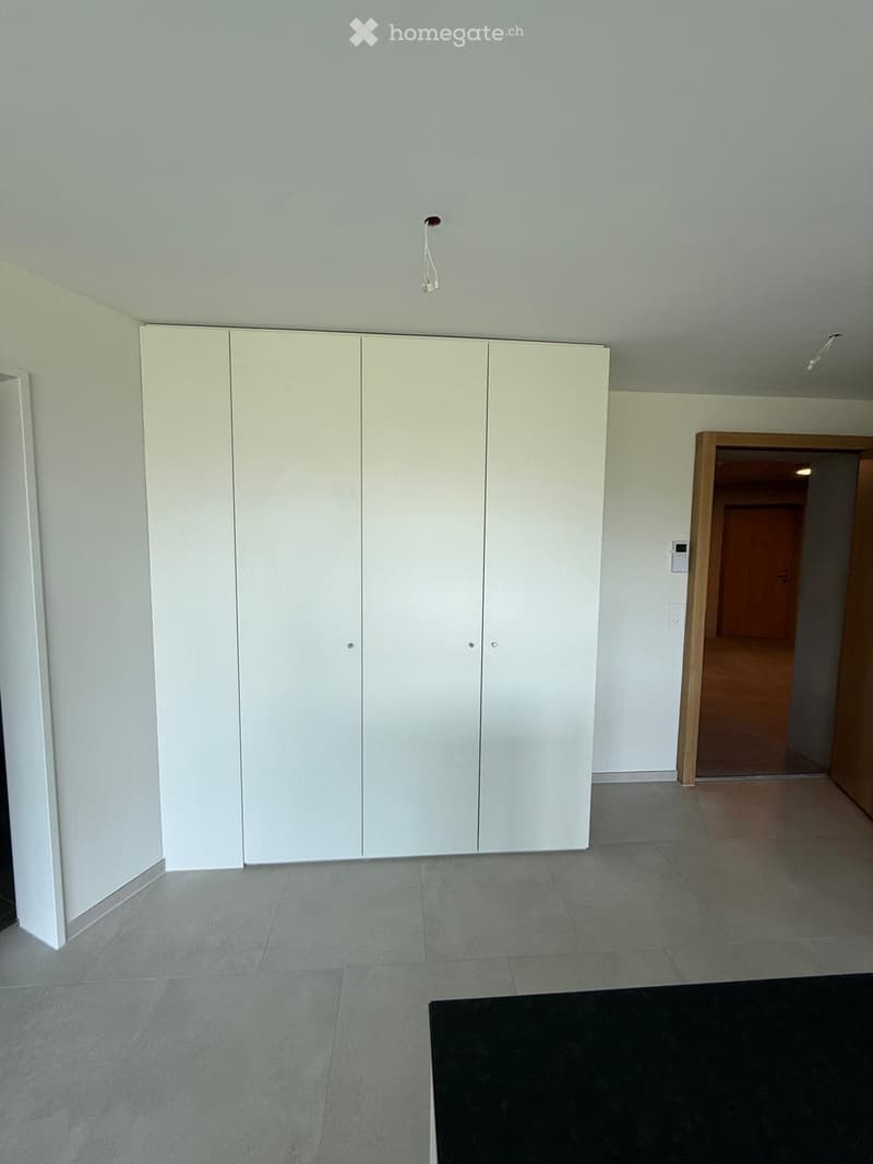 Empty room with white built-in wardrobes, grey tiled floor, and a doorway leading to another room.