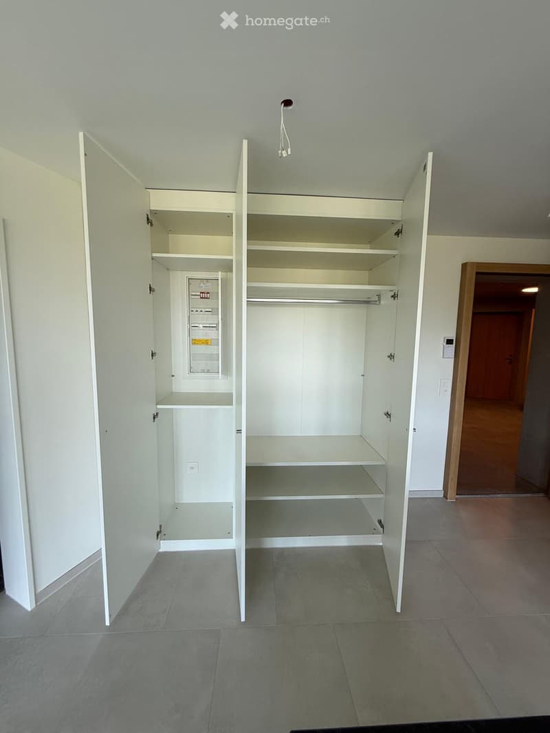 Empty room with white built-in closet and shelves, grey tiled floor, and a visible electrical panel.