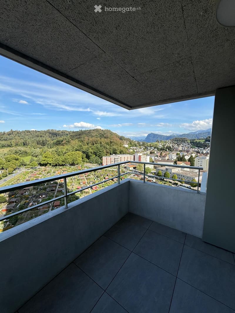 Modern balcony with grey tiled floor, metal railing, and expansive view of a town and surrounding mountains.