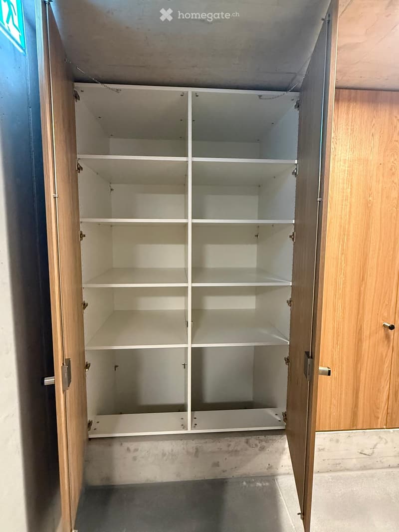 Empty closet with wooden doors and white shelves, no items inside.