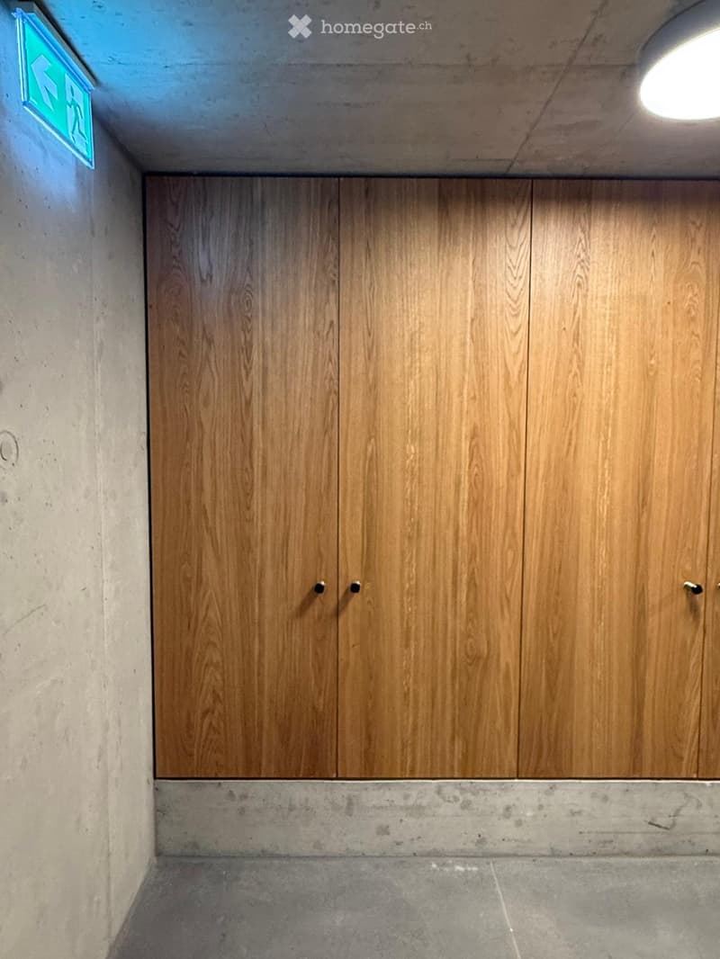 Empty hallway with wooden panel doors, concrete walls, and a tiled floor.