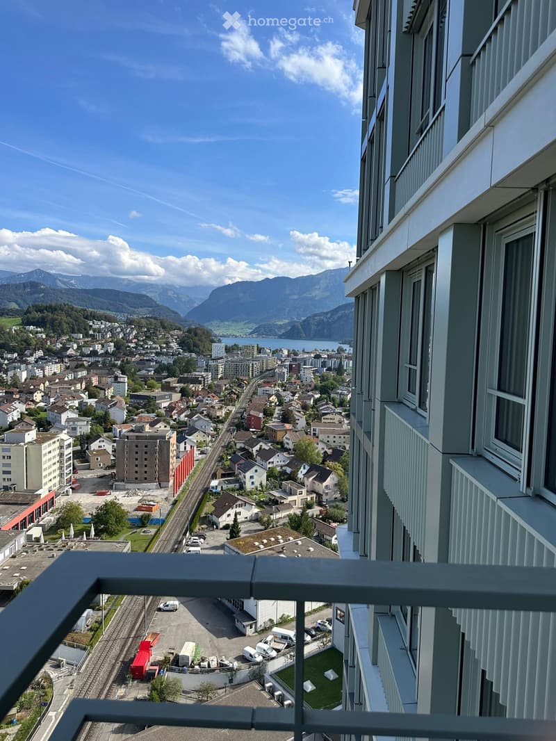 Balcony overlooking a town with houses, a lake, and mountains in the background.