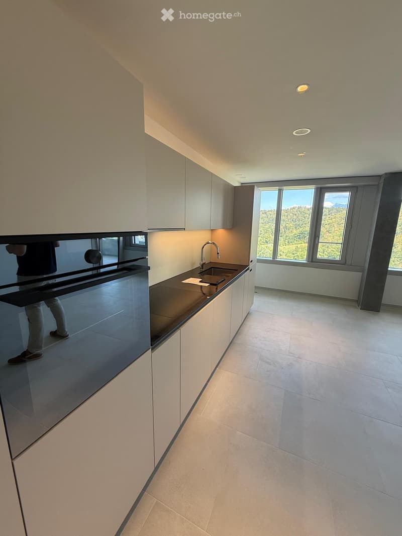 Modern kitchen with white cabinets, black countertops, and a large window overlooking a scenic view.