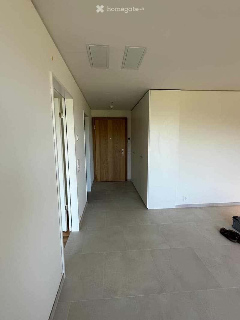 Empty hallway with tiled floor, white walls, and a wooden door at the end.