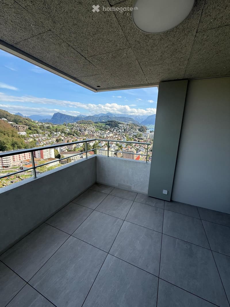 Modern balcony with tiled floor, metal railing, and expansive scenic view of a town and mountains.