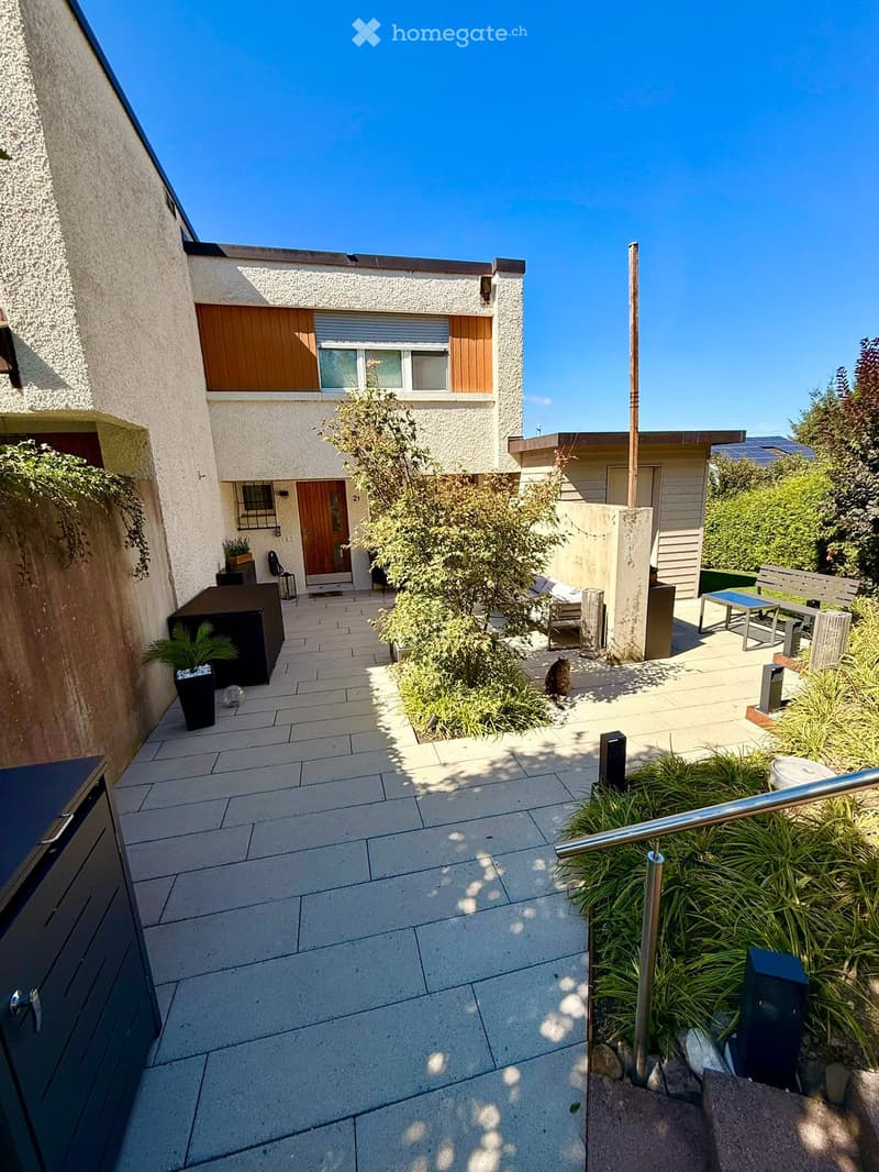 Courtyard with tiled pathway, small garden area, outdoor seating, and modern house entrance.