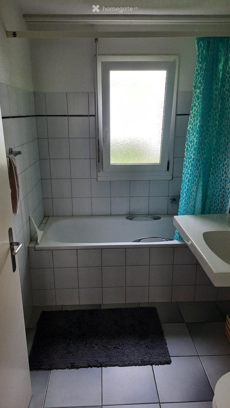 Bathroom with a bathtub, sink, towel, and a dark bathroom mat on the floor.