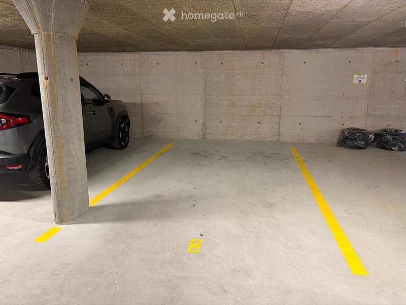 Underground parking area with concrete pillars, yellow parking lines, and a parked car in one of the designated spots.