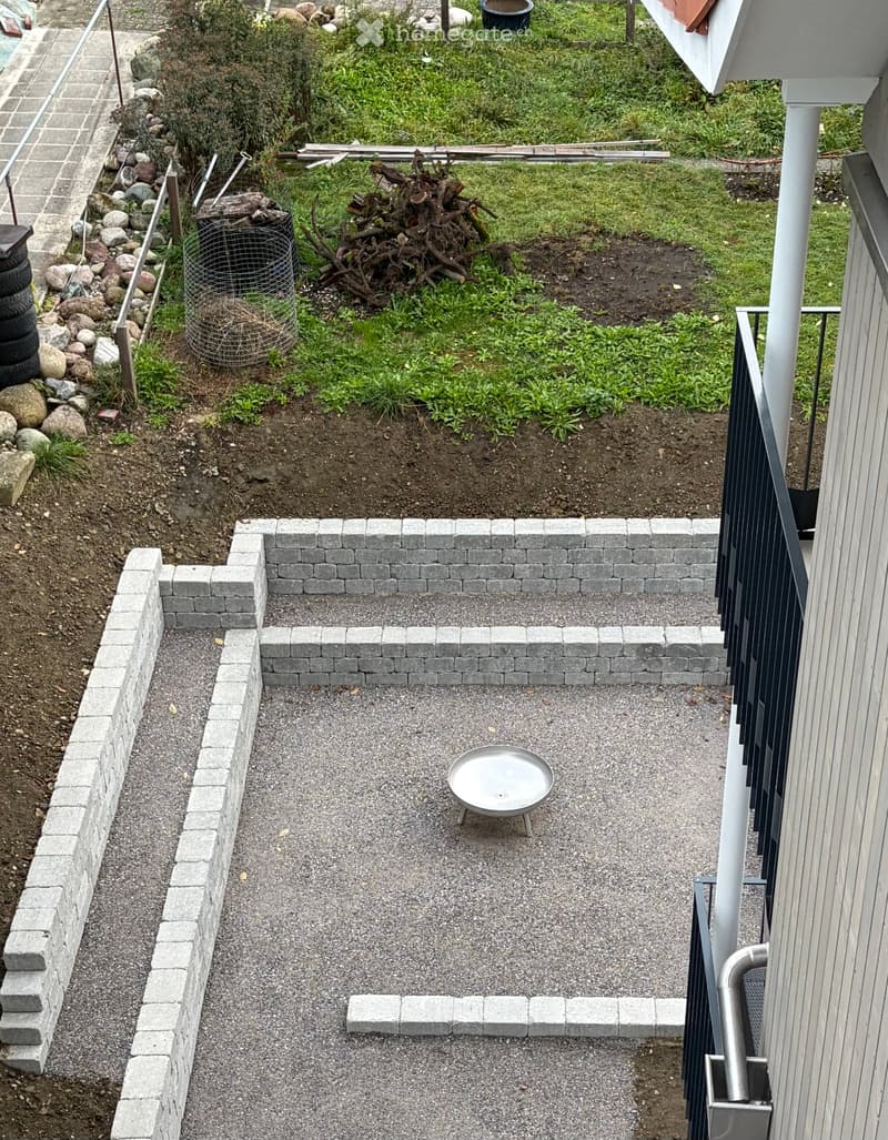 Small garden area with gravel pathway, raised stone border, and a metal bowl in the center.