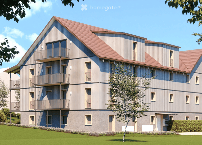 Modern multi-story residential building with a grey facade, red-tiled roof, and multiple balconies. The building features large windows and is surrounded by a well-maintained lawn and small trees.