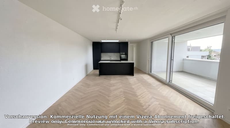 Open-plan space with a modern kitchen area featuring a black cabinet, island, sink, and oven, connected to a spacious living area with herringbone wooden flooring and large glass sliding doors leading to a balcony.