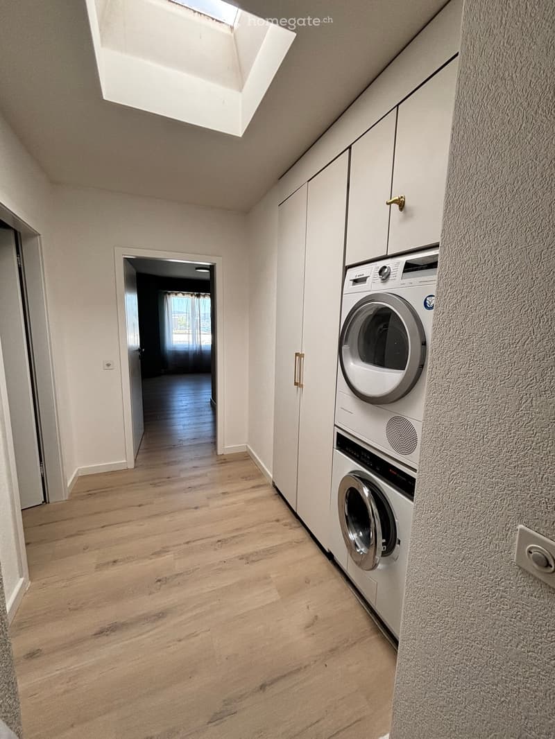 Hallway with wooden flooring, white walls, and a private washing machine and dryer unit on the right side.