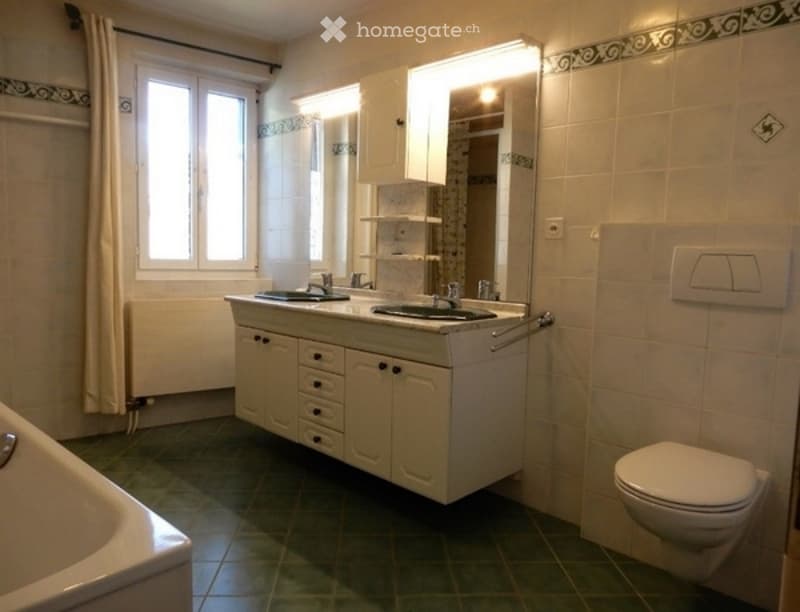 Bathroom with double sink vanity, mirror, toilet, bathtub, and tiled walls and floor.