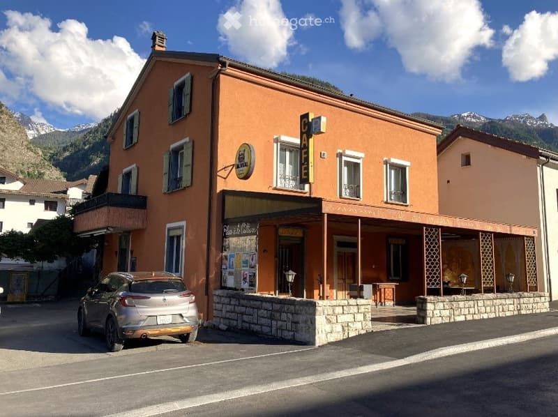 Two-story building with orange facade, multiple windows, and a sign reading "CAFE" above the entrance. A small outdoor seating area is visible in front.
