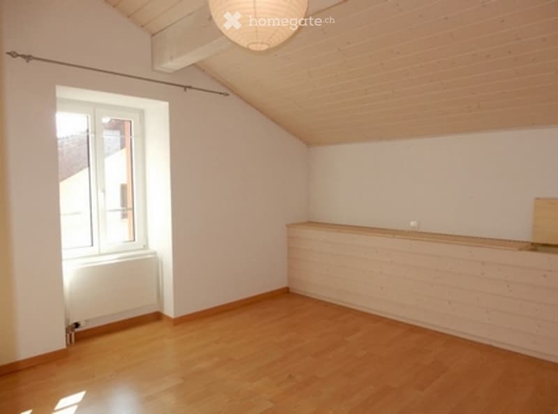 Empty attic room with wooden floors, white walls, and a skylight window. No furniture or equipment present.