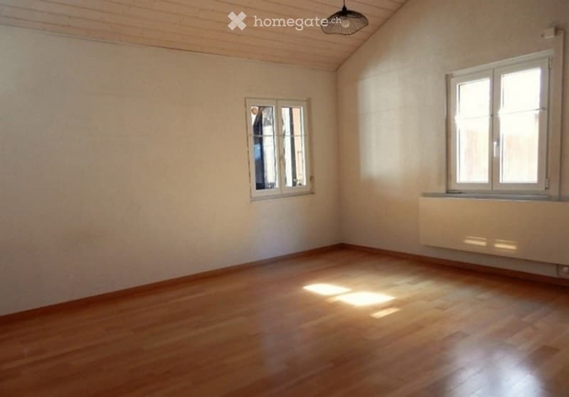 Empty room with wooden flooring, white walls, and two windows with white frames. Natural light streams in, illuminating the space.