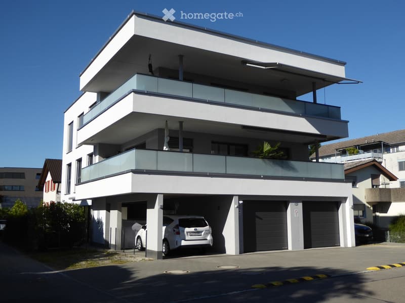 Modern two-story house with white exterior, large garage, and balconies with glass railings.