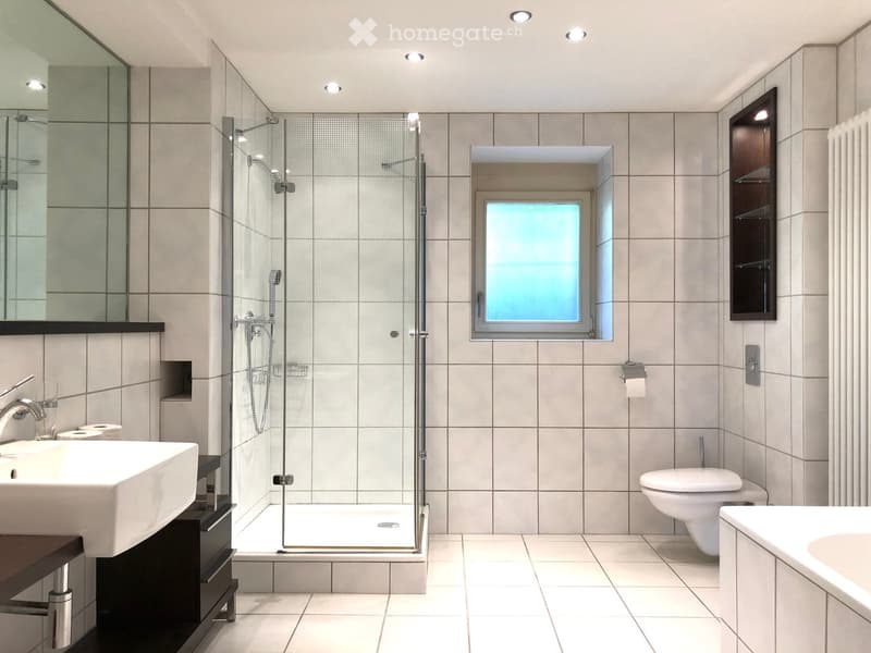 Modern bathroom with white tiles, a large sink, a bathtub, a toilet, a glass-enclosed shower, and a window with frosted glass.