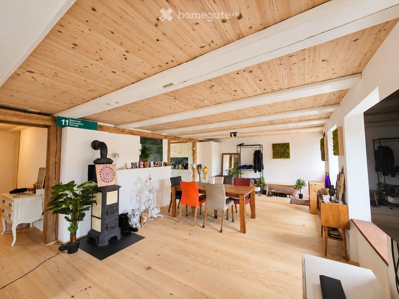 Open-plan living and dining area with wooden floors, exposed wooden beams, fireplace, dining table with chairs, cabinet, and decorative items.