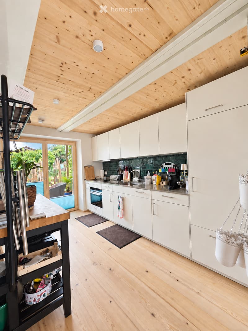 Modern kitchen with white cabinets, wooden countertops, and a sleek design. Features include a sink, oven, and various kitchen utensils. The space is well-lit with natural light from the large window and has a cozy, inviting atmosphere.