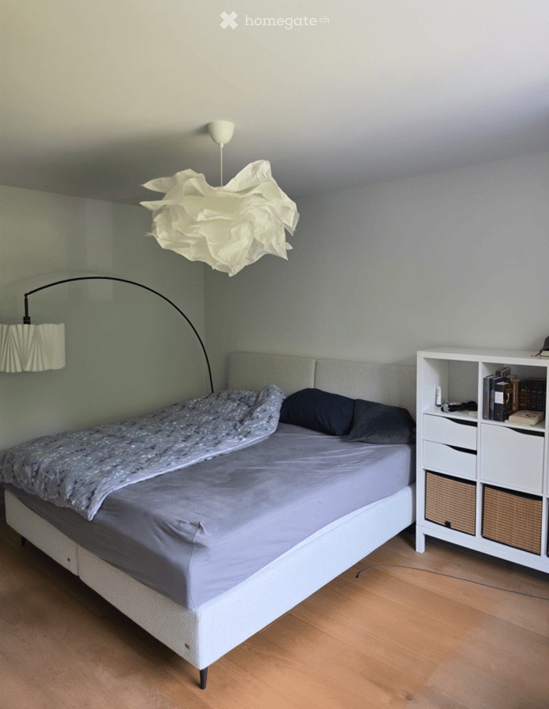 A modern bedroom with a large bed, a nightstand, a bookshelf, and decorative lighting.