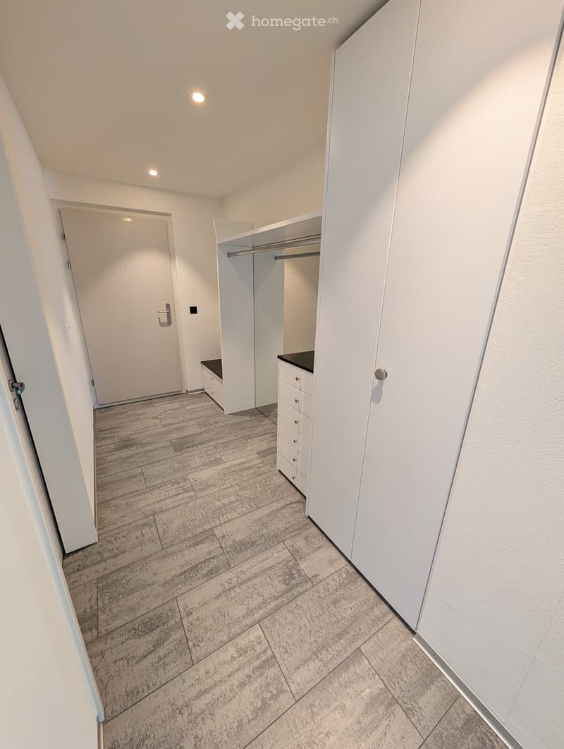 Empty hallway with white walls, tiled floor, built-in closet with drawers, and a closed door at the end.